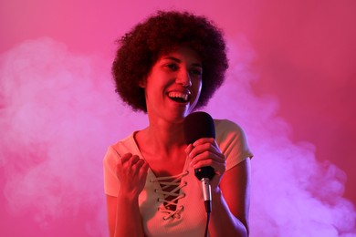Photo of Curly young woman with microphone singing on pink background. Color tone effect