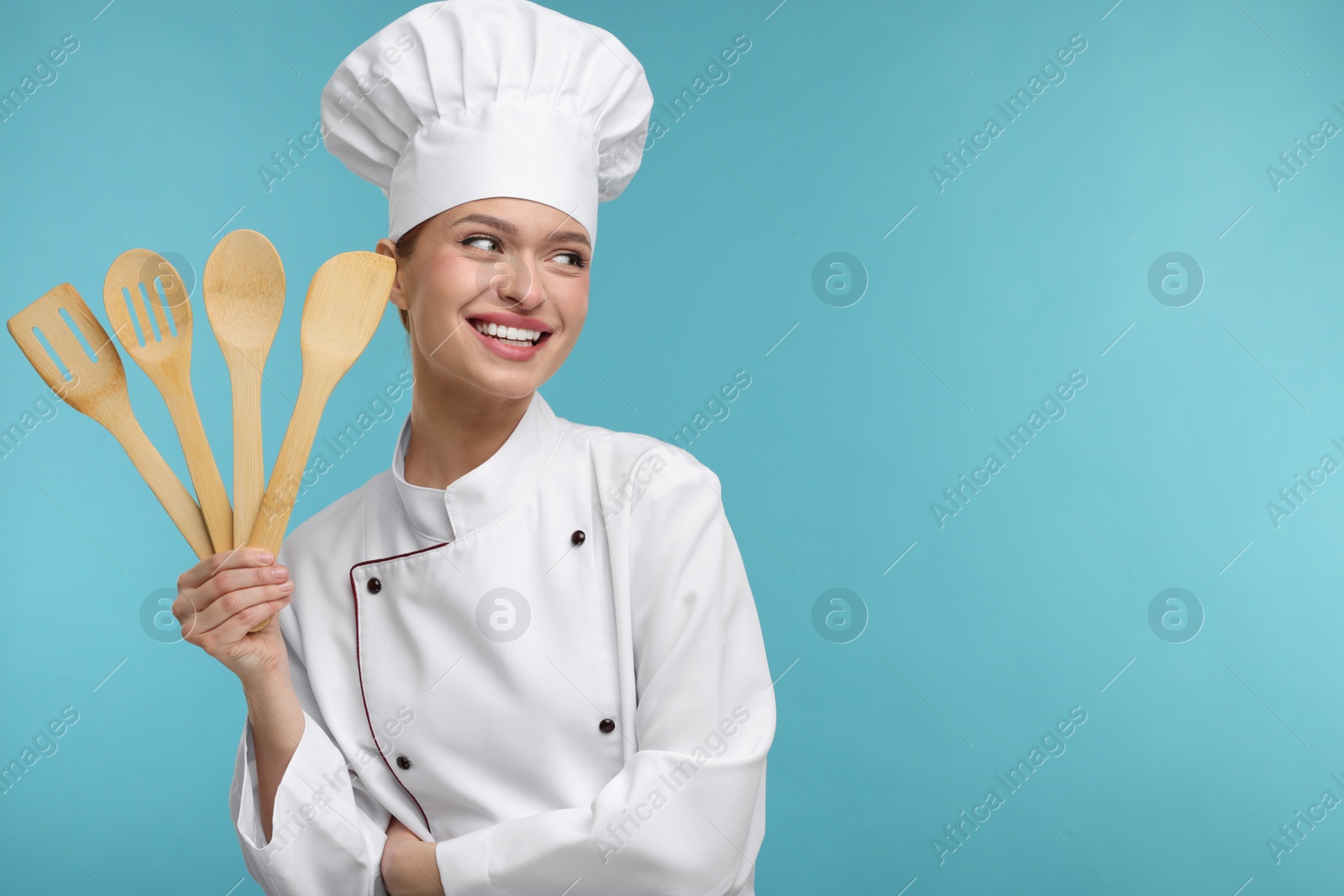 Photo of Happy woman chef in uniform holding wooden utensils on light blue background, space for text