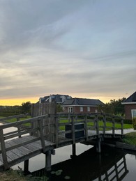 Photo of Canal, wooden bridge, lawn and houses under beautiful sky