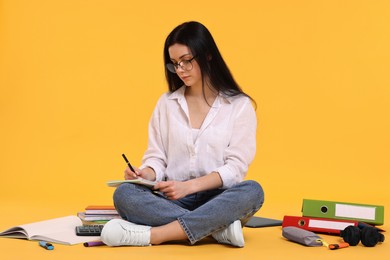 Photo of Student writing in notebook among books and stationery on yellow background
