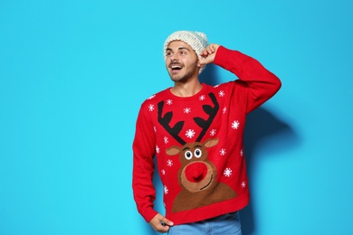 Young man in Christmas sweater and knitted hat on color background