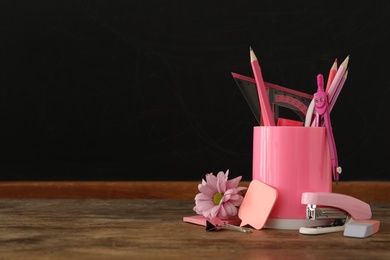 Set of stationery and flower on wooden table near chalkboard, space for text. Teacher's Day