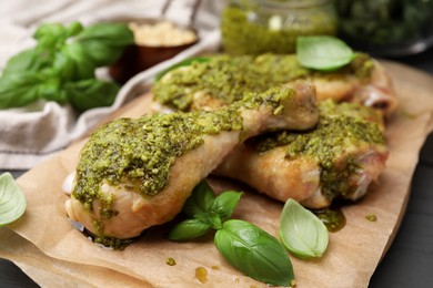 Delicious fried chicken drumsticks with pesto sauce and basil on table, closeup