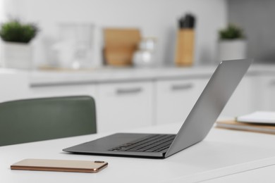 Photo of Home office. Laptop and smartphone on white desk in kitchen, space for text