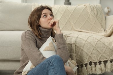 Photo of Sad young woman sitting near sofa at home