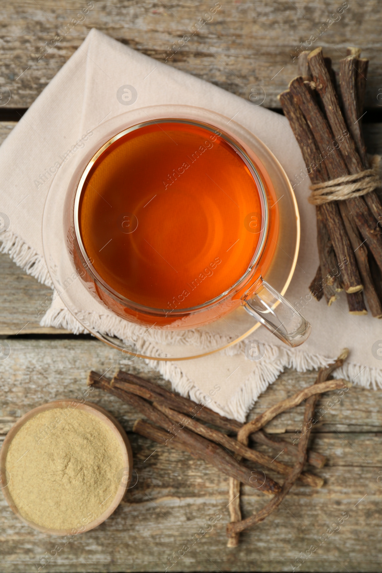 Photo of Aromatic licorice tea in cup, dried sticks of licorice root and powder on wooden table, flat lay