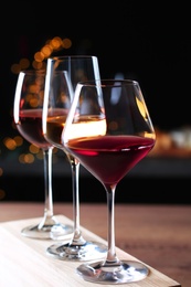 Photo of Glasses with different wines on wooden table against defocused lights