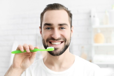 Young man brushing his teeth indoors