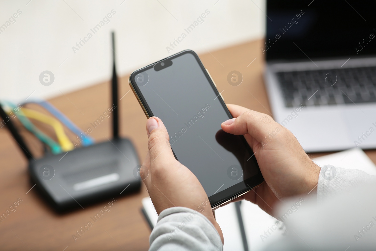 Photo of Man with smartphone and laptop connecting to internet via Wi-Fi router at wooden table, closeup