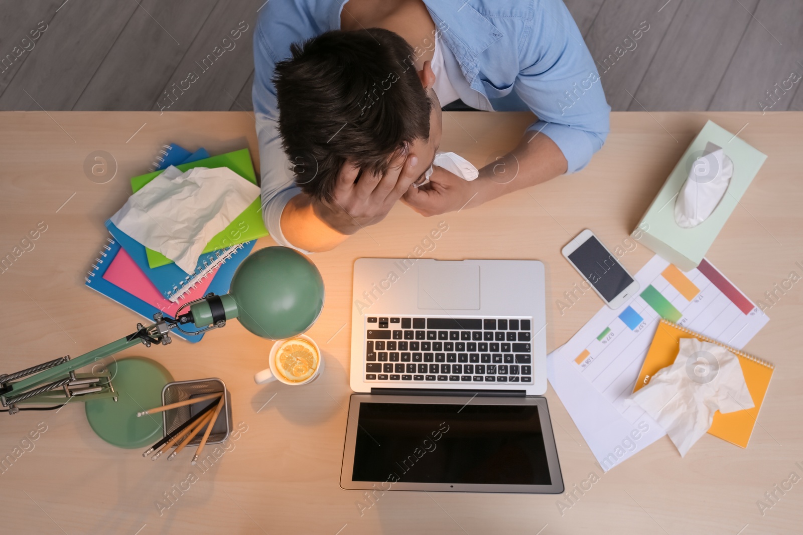 Photo of Exhausted man with tissue suffering from cold while working with laptop at table, top view