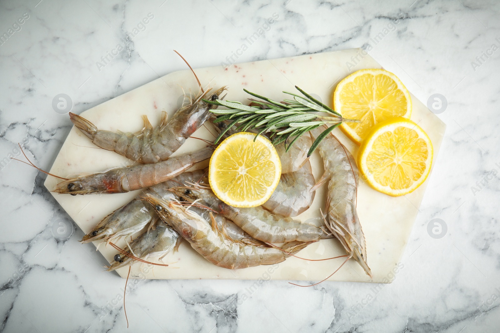 Photo of Raw shrimps with lemon slices and rosemary on marble table, top view