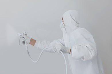 Photo of Decorator in uniform painting white wall with spray