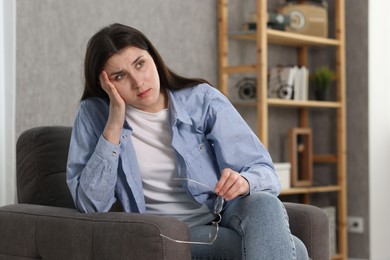 Photo of Overwhelmed woman with glasses sitting in armchair at home