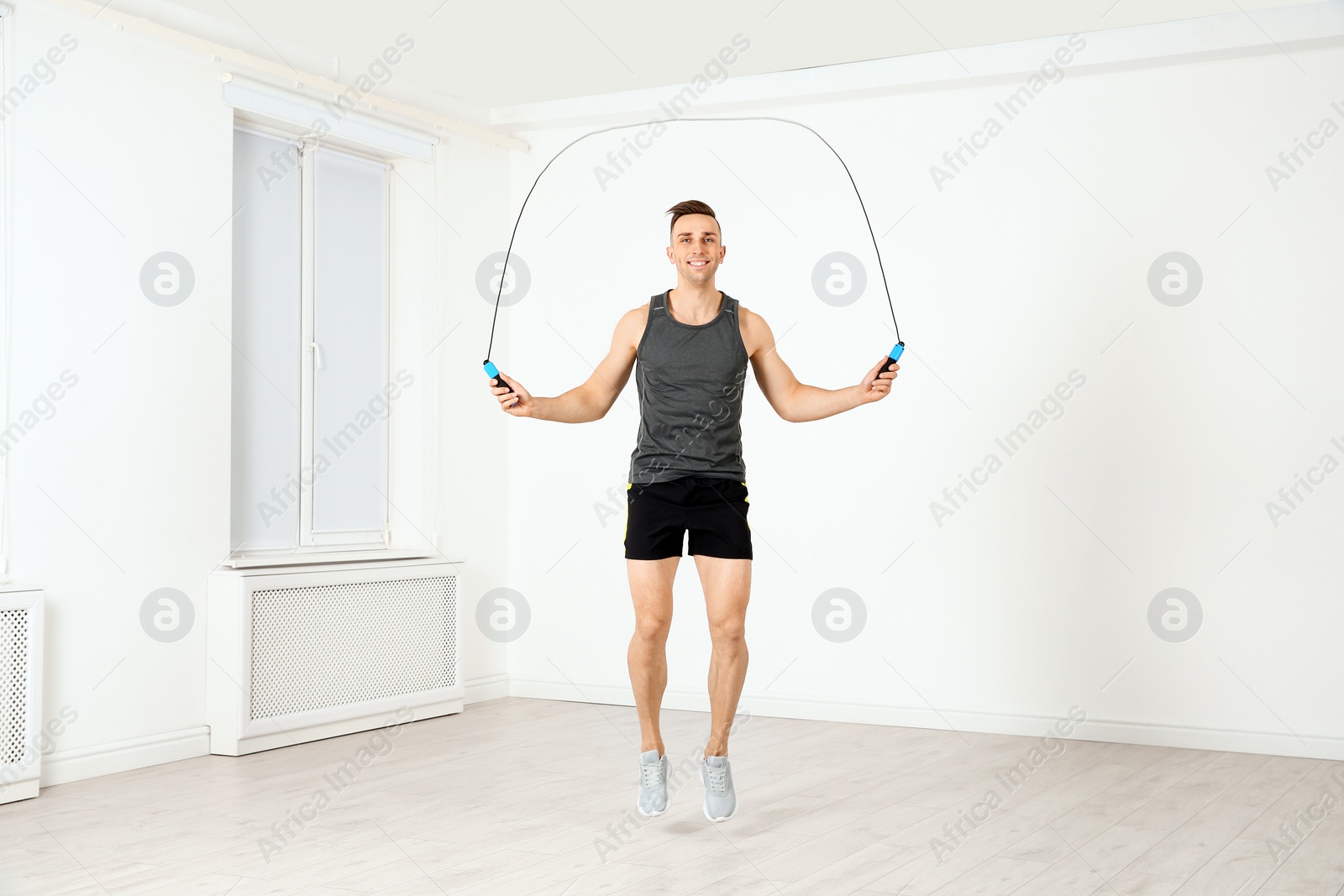 Photo of Full length portrait of young sportive man training with jump rope in light room