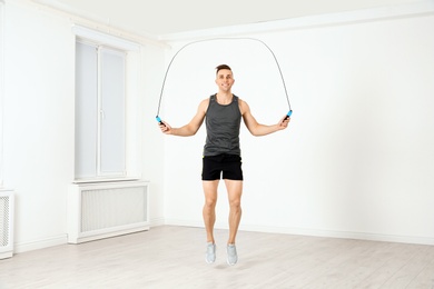 Full length portrait of young sportive man training with jump rope in light room