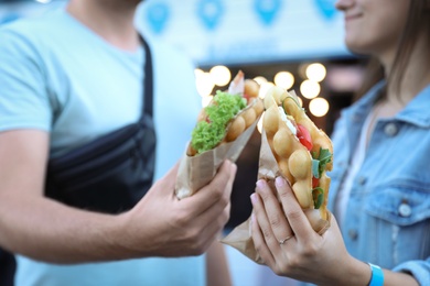 Photo of Young couple holding delicious bubble waffles with tomato and arugula outdoors, closeup