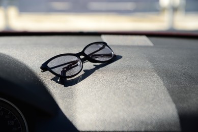 Stylish glasses on dashboard in car, space for text