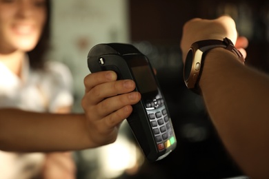 Man using terminal for contactless payment with smart watch in cafe, closeup