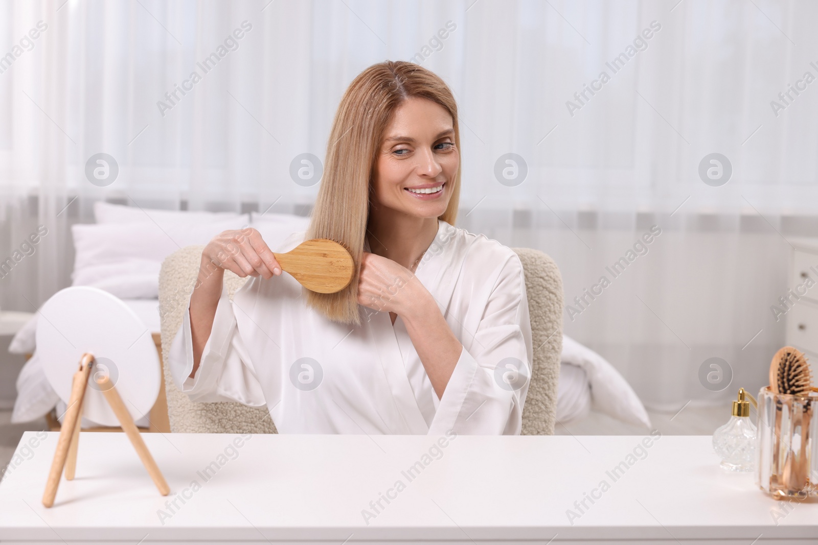 Photo of Beautiful woman brushing her hair at vanity in bedroom