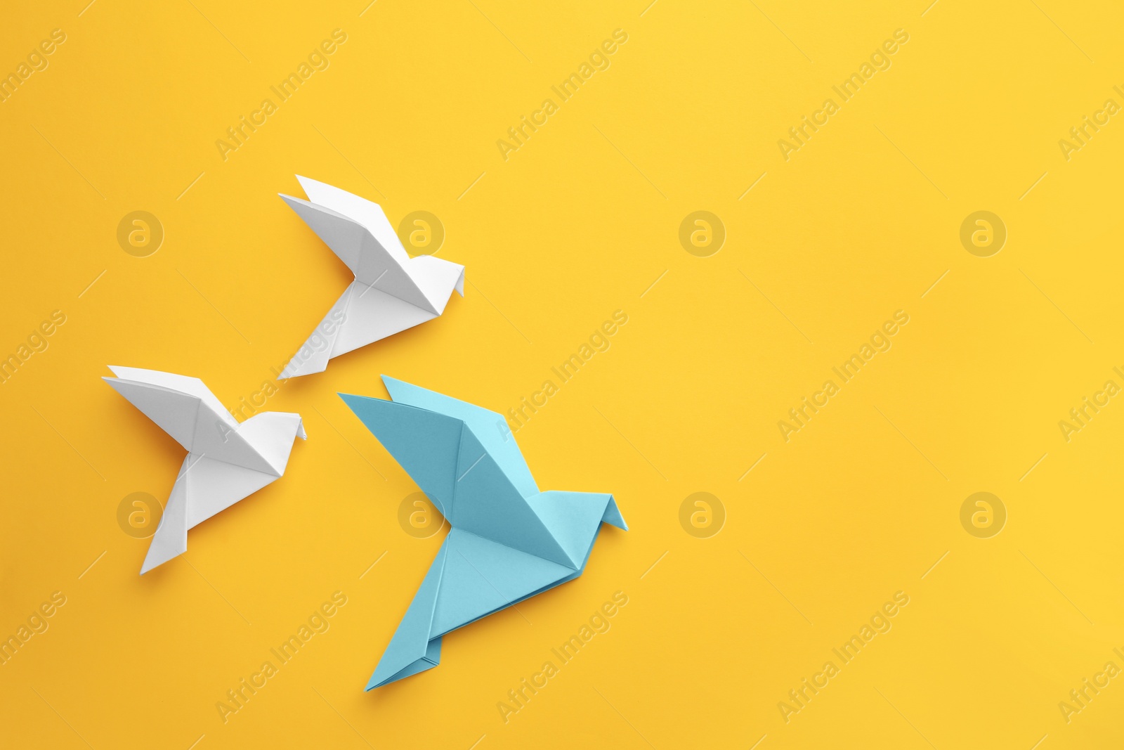 Photo of Origami art. Colorful handmade paper birds on yellow background, flat lay. Space for text