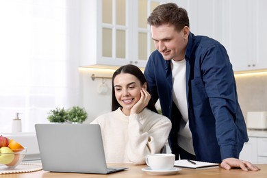 Happy couple using laptop together at wooden table in kitchen