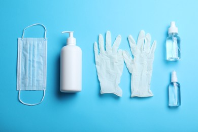 Medical gloves, mask and hand sanitizers on light blue background, flat lay