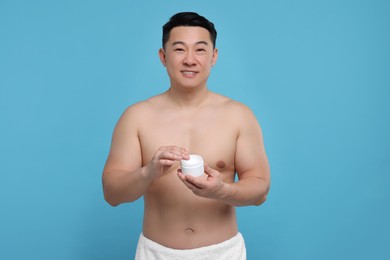 Handsome man with jar of body cream on light blue background