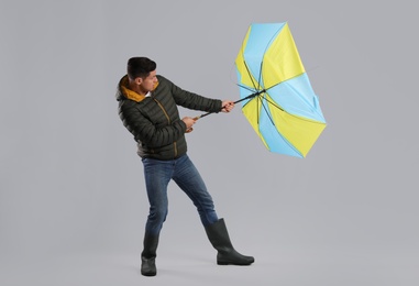Man with umbrella caught in gust of wind on grey background
