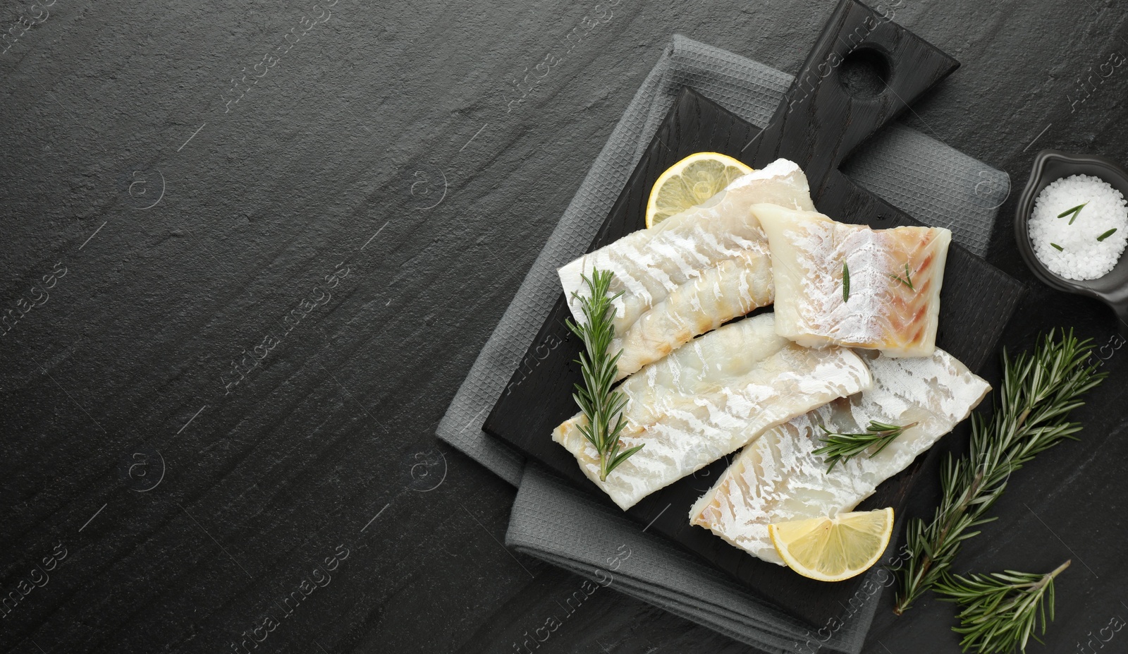 Photo of Fresh raw cod fillets, rosemary, lemon and salt on black table, flat lay. Space for text