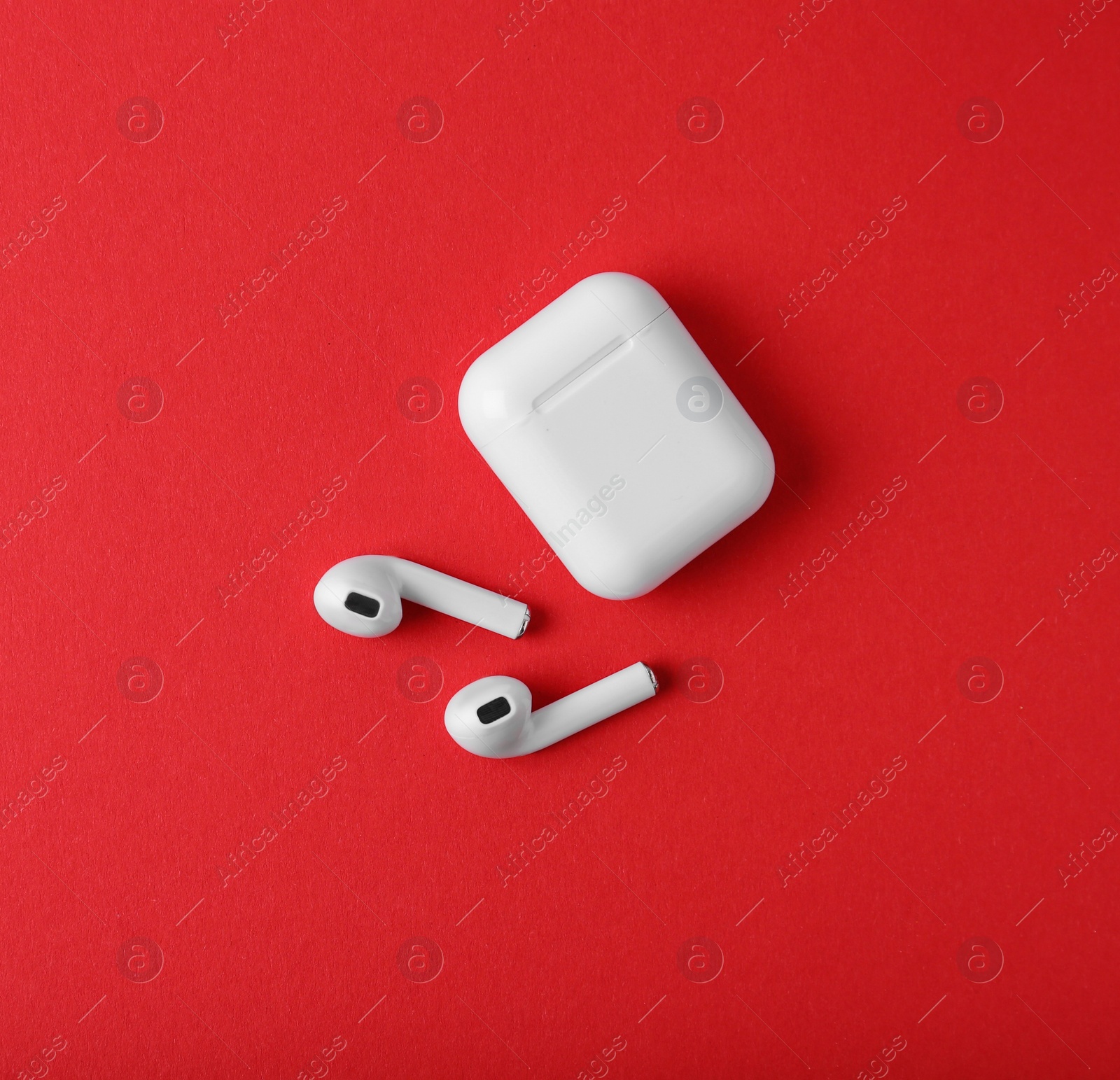 Photo of Modern wireless earphones and charging case on red background, flat lay. Space for text