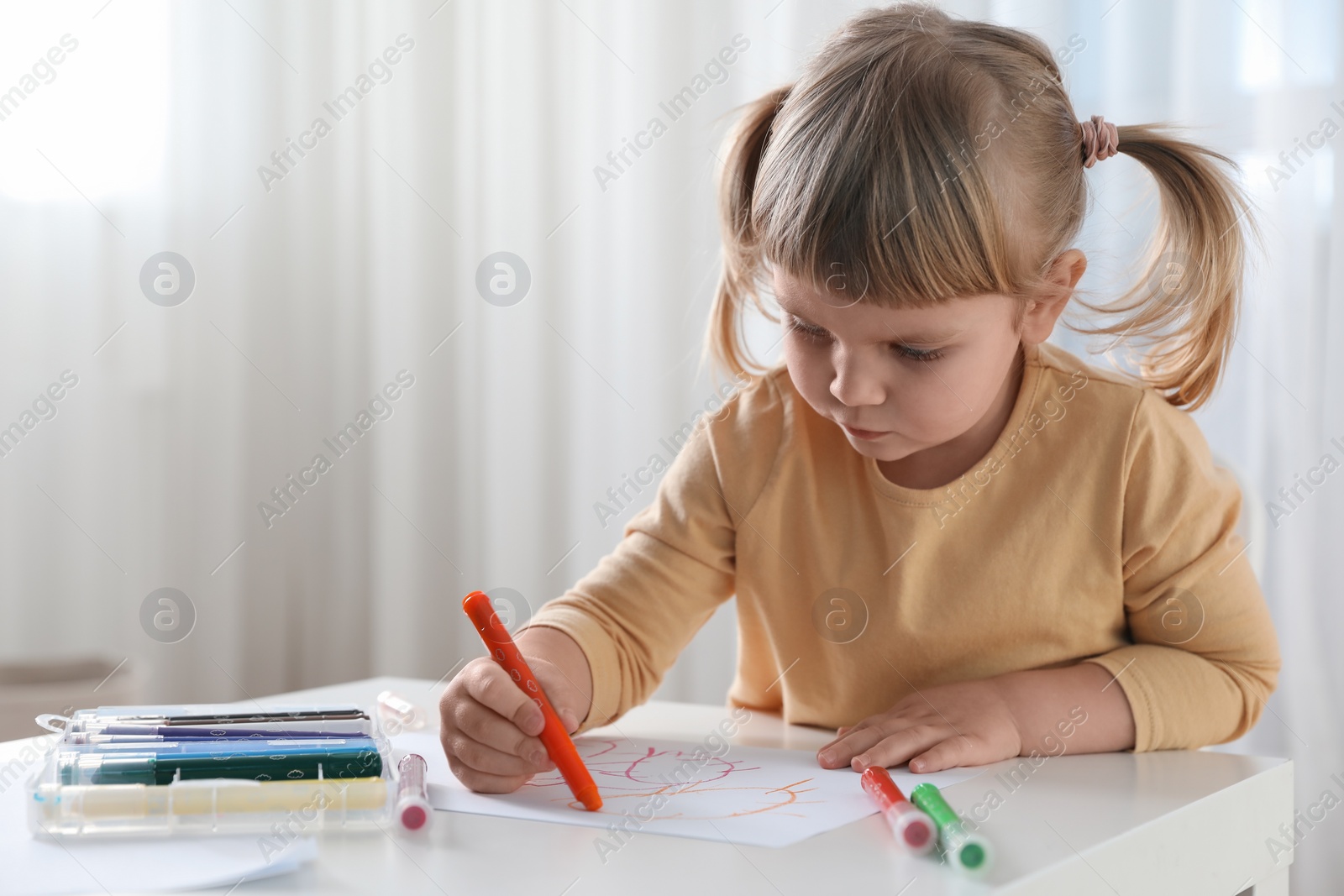 Photo of Cute little girl drawing with marker at white table indoors. Child`s art