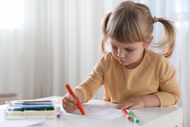 Cute little girl drawing with marker at white table indoors. Child`s art