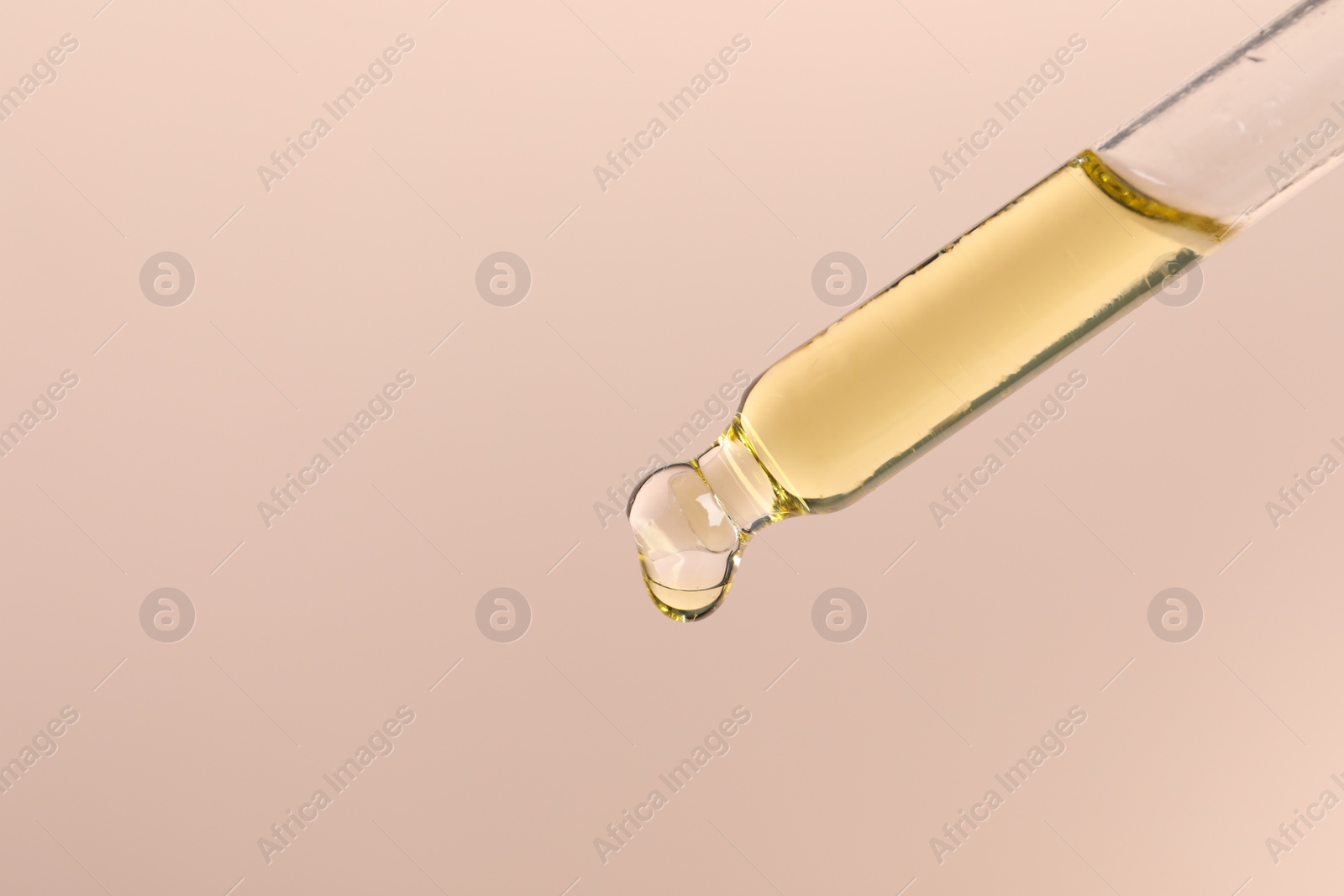 Photo of Dripping cosmetic serum from pipette on beige background, space for text