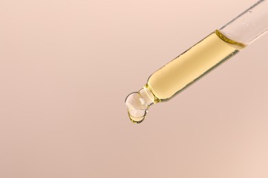 Dripping cosmetic serum from pipette on beige background, space for text