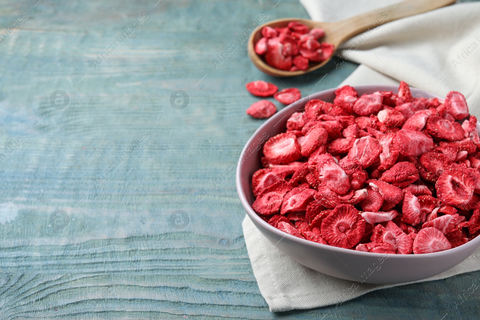 Photo of Bowl and spoon with dried strawberries on light blue wooden table. Space for text