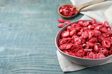 Photo of Bowl and spoon with dried strawberries on light blue wooden table. Space for text