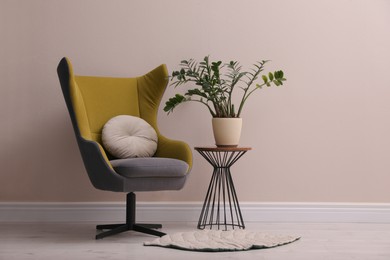 Comfortable armchair and beautiful plant near light wall indoors