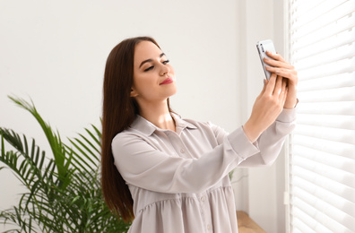 Beautiful woman taking selfie near window indoors