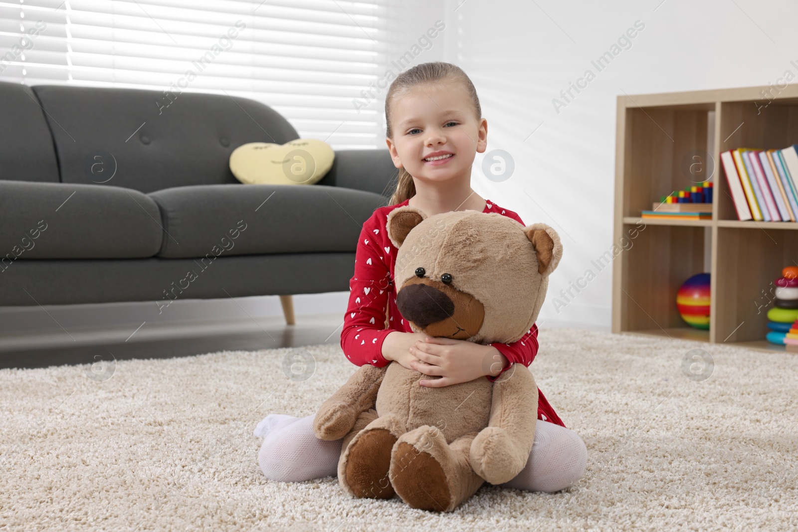 Photo of Cute little girl playing with teddy bear at home