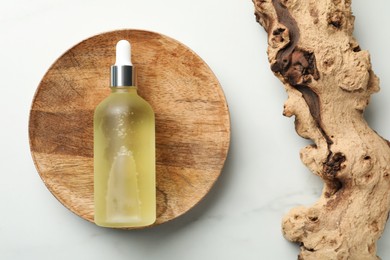 Photo of Wooden plate with bottle of hydrophilic oil near tree bark on white background, flat lay