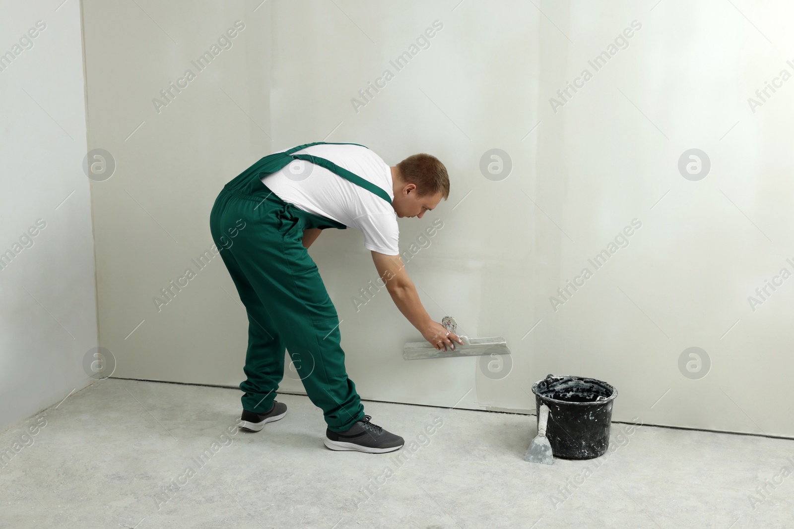 Photo of Professional worker plastering wall with putty knife indoors