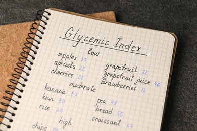 Photo of List with products of low, moderate and high glycemic index in notebook on grey table, closeup