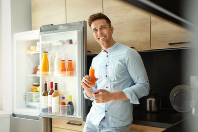 Photo of Man with bottle of juice near refrigerator in kitchen
