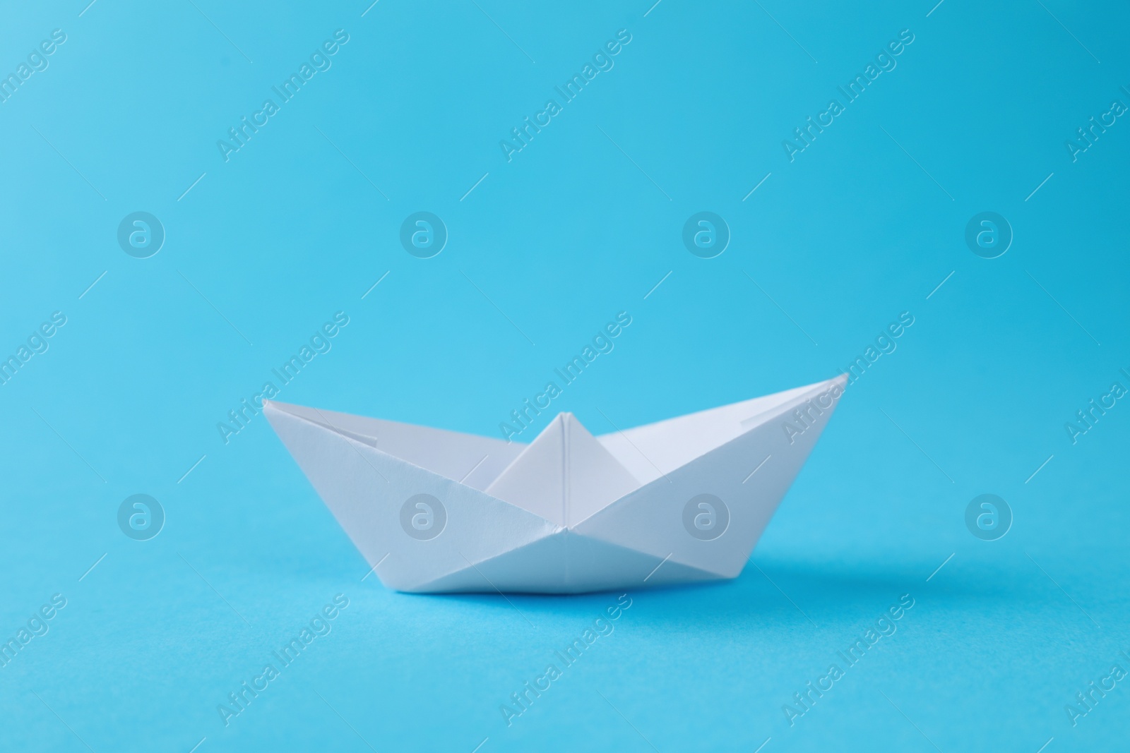 Photo of Handmade white paper boat on light blue background. Origami art