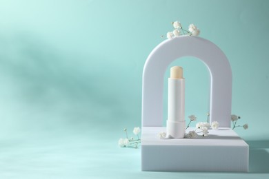 Photo of Stylish presentation of lip balm with gypsophila on light blue background, space for text