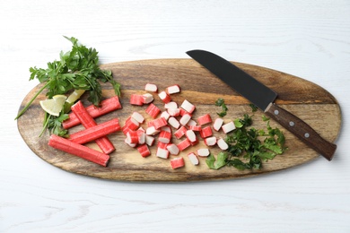 Delicious crab sticks with parsley, lemon and knife on white wooden table, top view