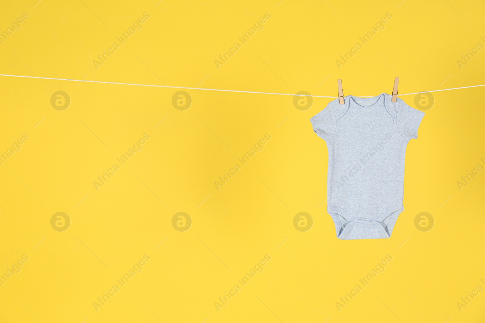 Photo of Baby onesie hanging on clothes line against yellow background, space for text