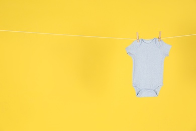 Photo of Baby onesie hanging on clothes line against yellow background, space for text