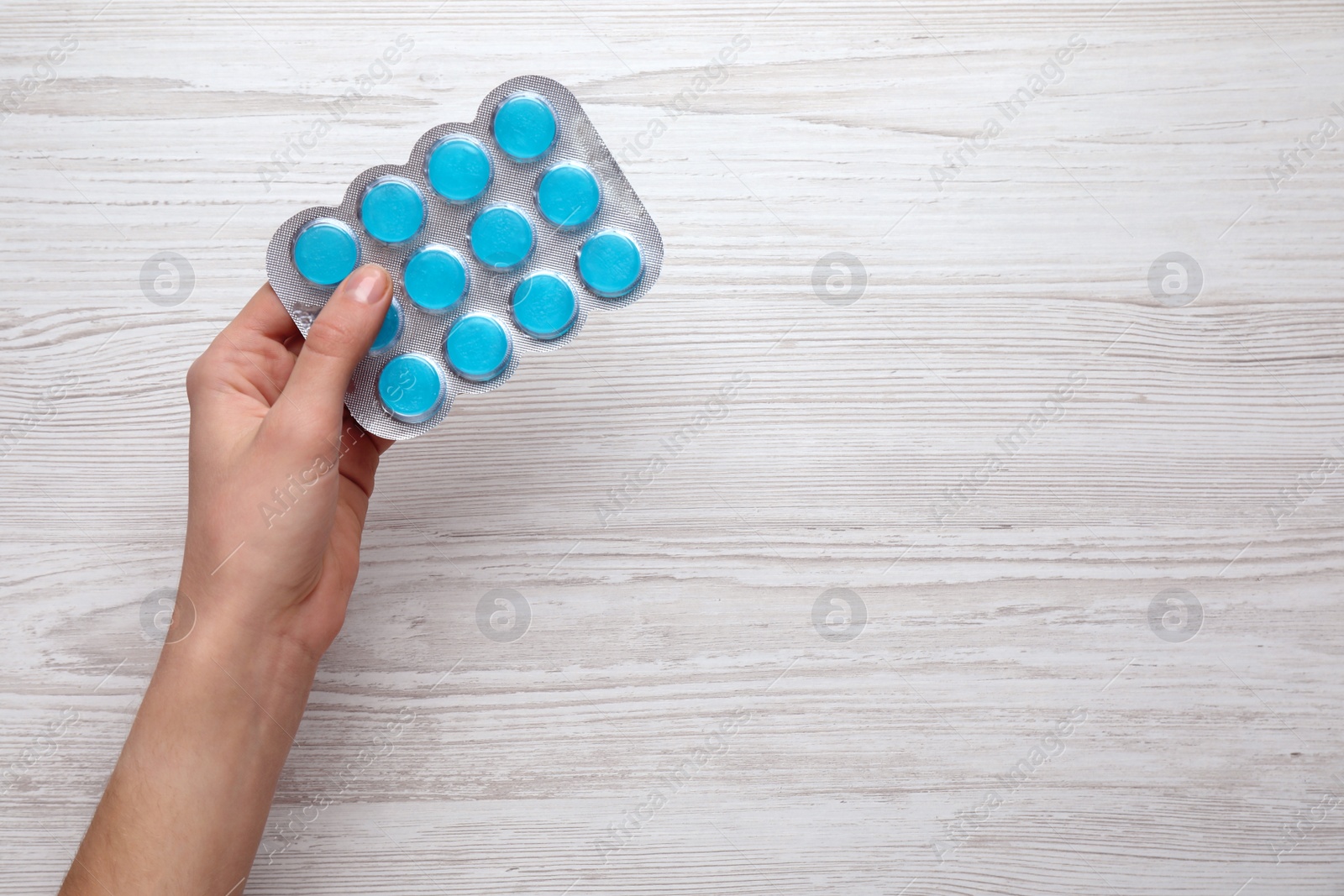 Photo of Woman holding blister with cough drops on white wooden background, top view. Space for text