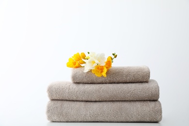 Photo of Stack of fresh towels with flowers on table against white background